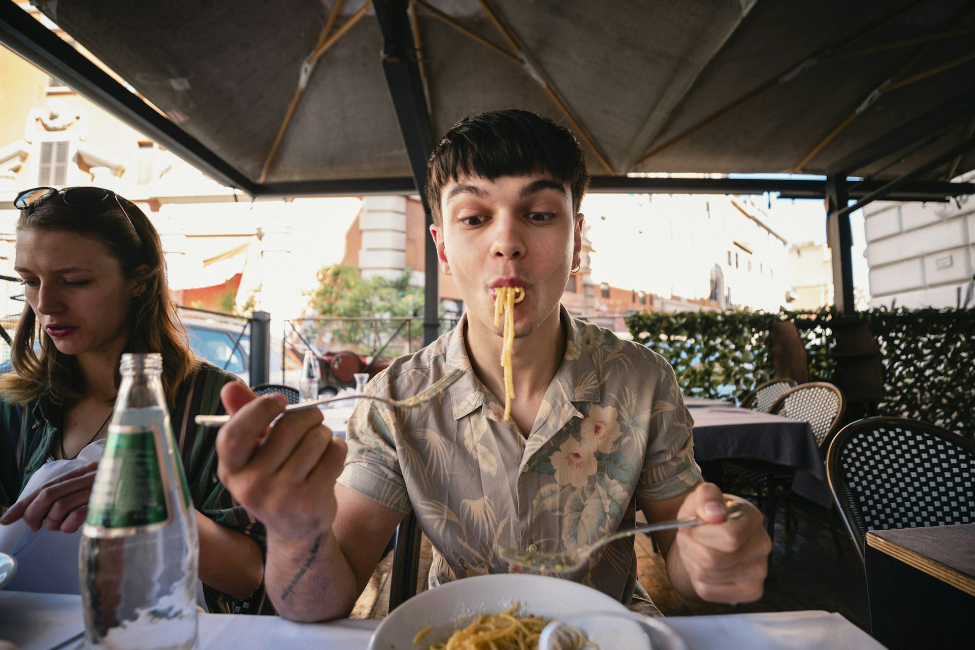 A front-view shot of a young man enjoying a delicious meal of spaghetti in Italy, he is wearing casual clothing